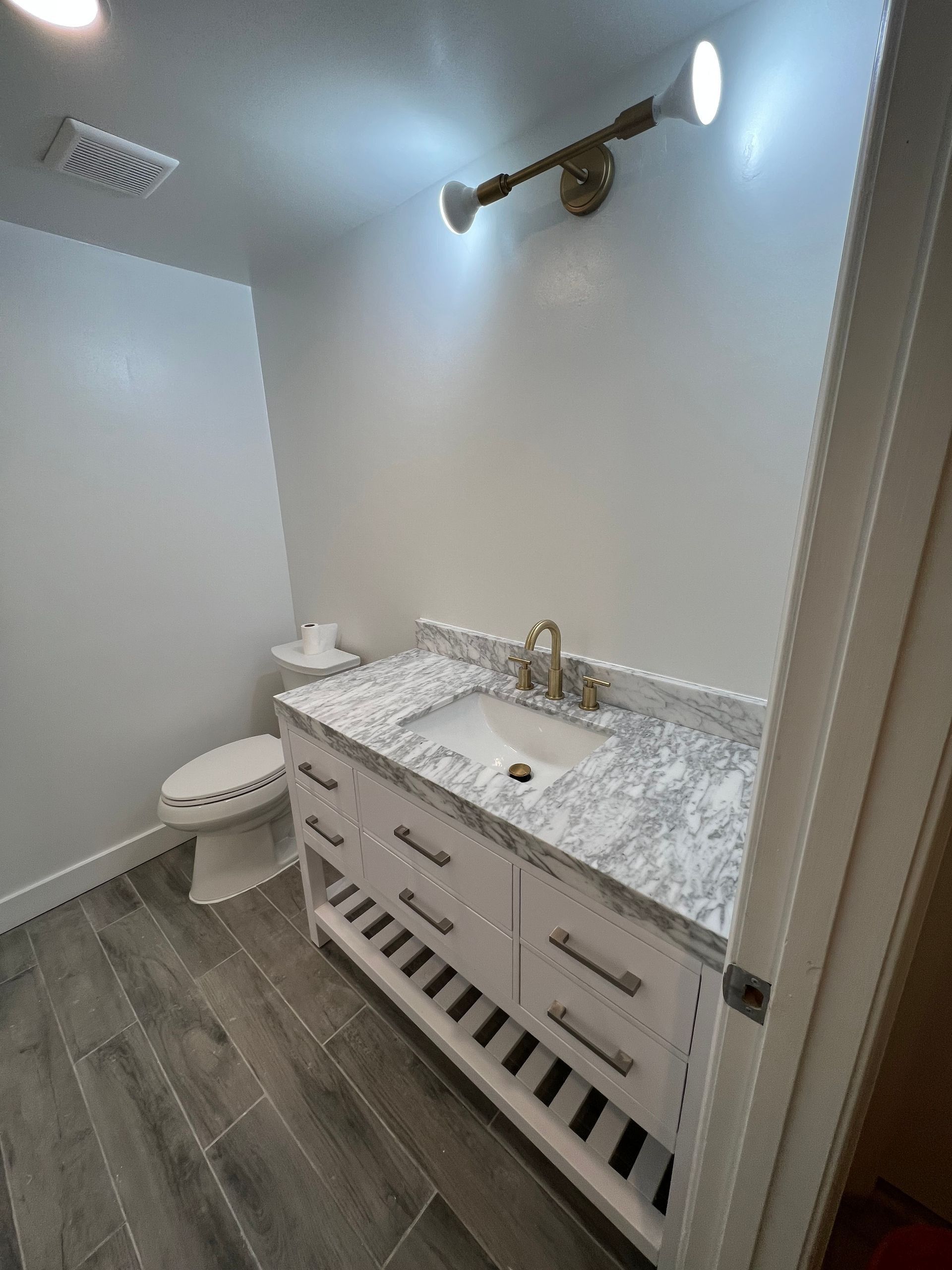 Small modern bathroom with a marble vanity, wall light, toilet, and gray tile floor.
