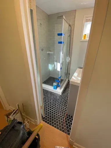 Small bathroom with a glass shower enclosure and black-and-white hex tile floor.