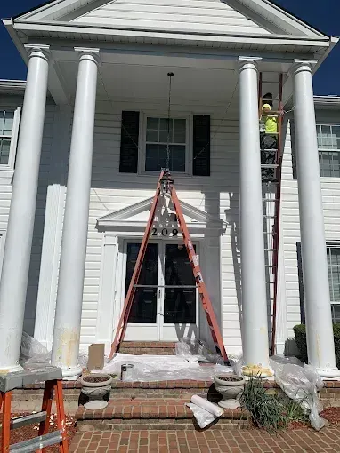 White house facade with tall columns, ladder on the front porch, and scattered construction materials.