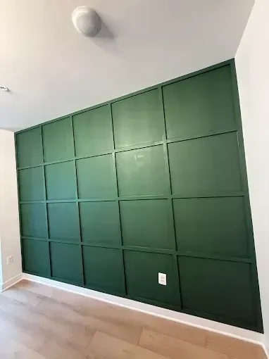 Green paneled accent wall in a bright empty room with light wood floors and a ceiling light
