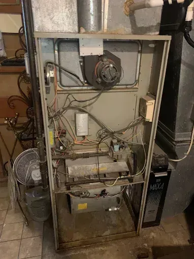 Open metal furnace cabinet with exposed wiring and components in a basement utility area