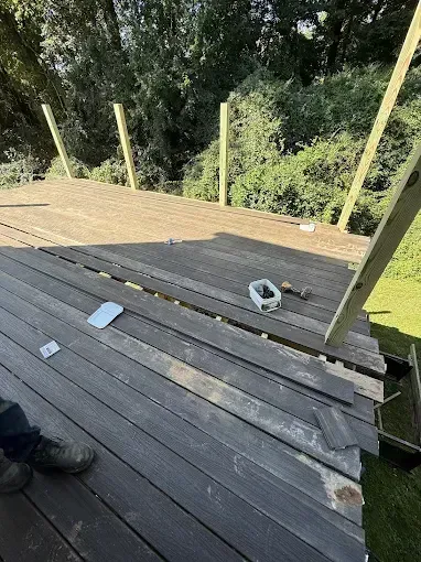 Wooden deck under construction with stacked planks, tools, and railing posts overlooking trees