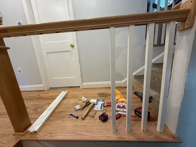 Wooden stair railing under construction with tools scattered on the floor and loose balusters nearby