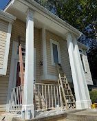 Front porch of a white house with columns and a chair leaning against the railing