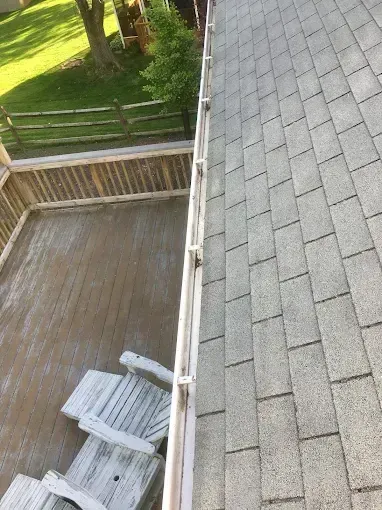 Roof viewed from above beside a wooden deck and fenced yard, with gray shingles and stacked boards below