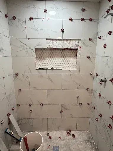 Tiled bathroom shower under construction with red tile spacers and a bucket on the floor