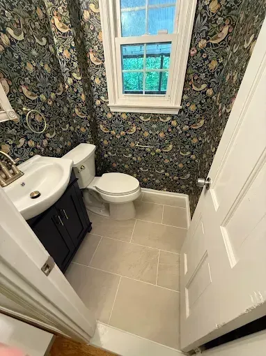 Small bathroom with floral wallpaper, white toilet, sink vanity, and a window above the toilet.