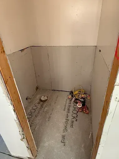 Small empty alcove with gray floor, white walls, and a pile of trash in the back right corner.