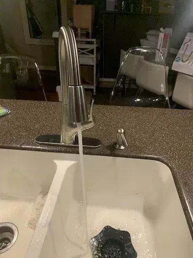 Kitchen sink with running faucet and a sponge in the basin.