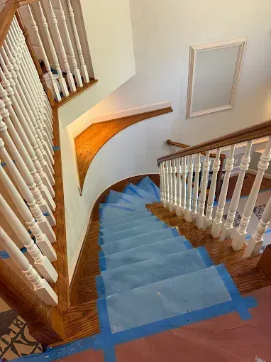 Wooden staircase with blue carpet runner and white railing descending in a curved hallway