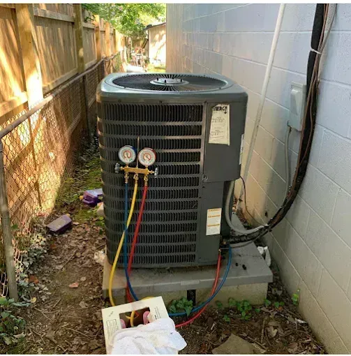 Outdoor air conditioner condenser beside a house, with gauges and hoses attached, in a narrow backyard alley