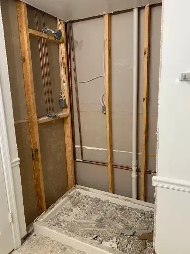 Bathroom wall under renovation with exposed studs, wiring, and debris on the floor