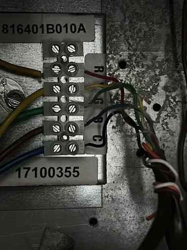 Close-up of a metal terminal block with multiple colored wires connected and labeled screws.