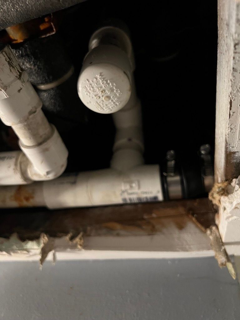 Under-sink plumbing pipes and drain lines inside a cabinet opening