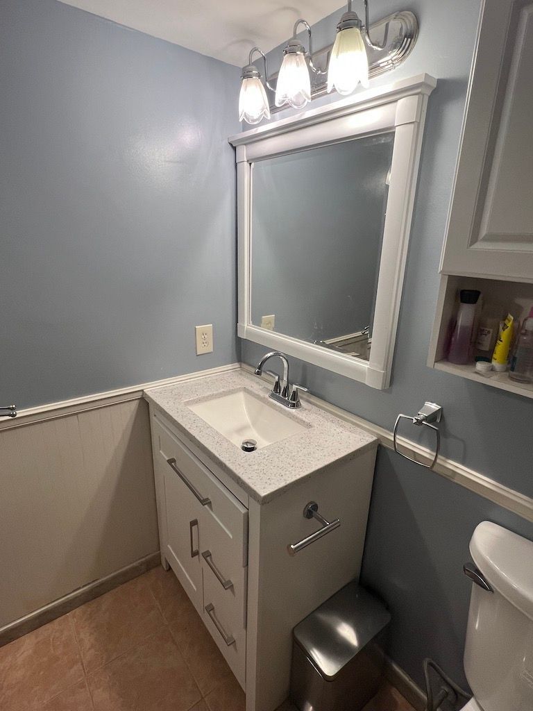 Small gray bathroom with a white vanity, large mirror, and three-light fixture above the sink.
