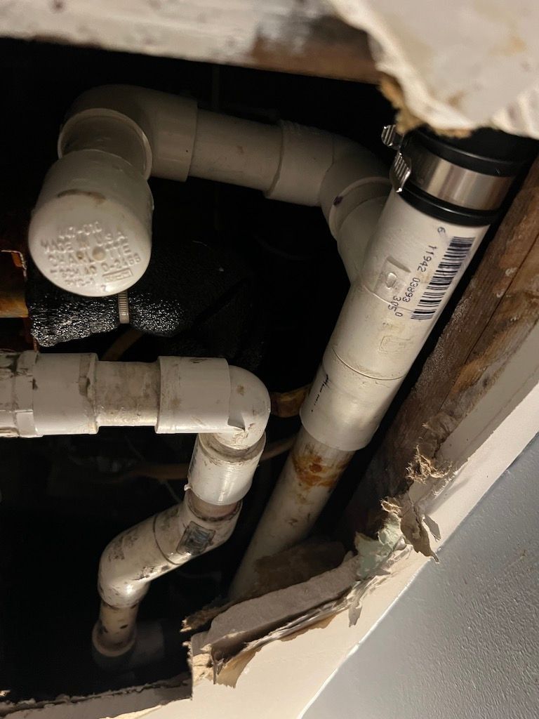 Close-up of white PVC plumbing pipes and fittings inside a dark wall cavity with damaged drywall.