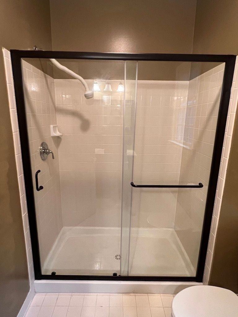 Glass shower stall with black frame, chrome fixtures, and white shower base in a bathroom