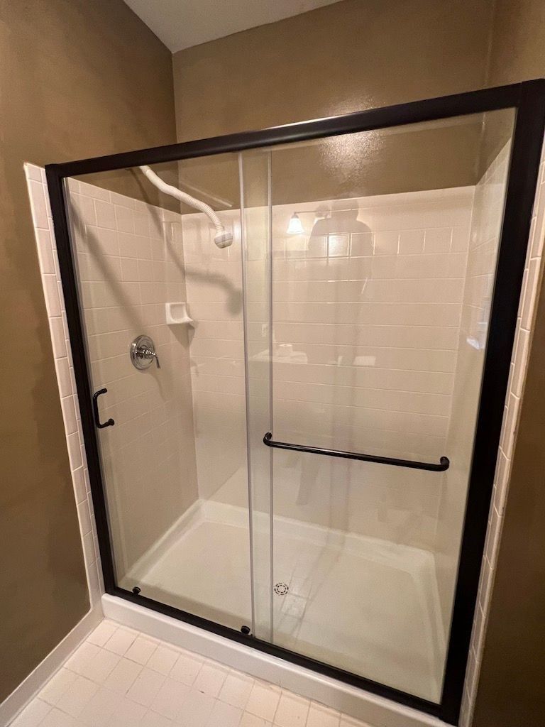 Glass walk-in shower with black frame, built-in seat, and beige tiled bathroom walls