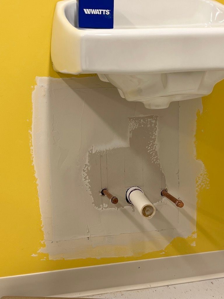 Partially installed wall-mounted sink with exposed plumbing against a yellow wall