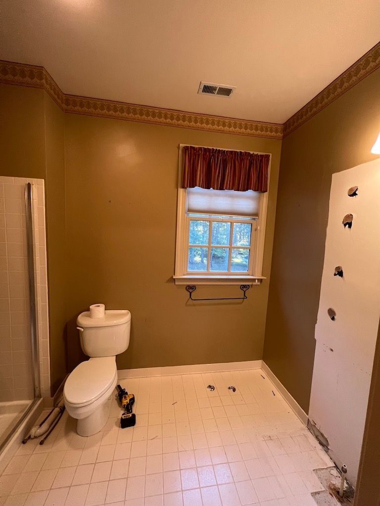 Small bathroom with toilet, shower, window, and white tiled floor under renovation.