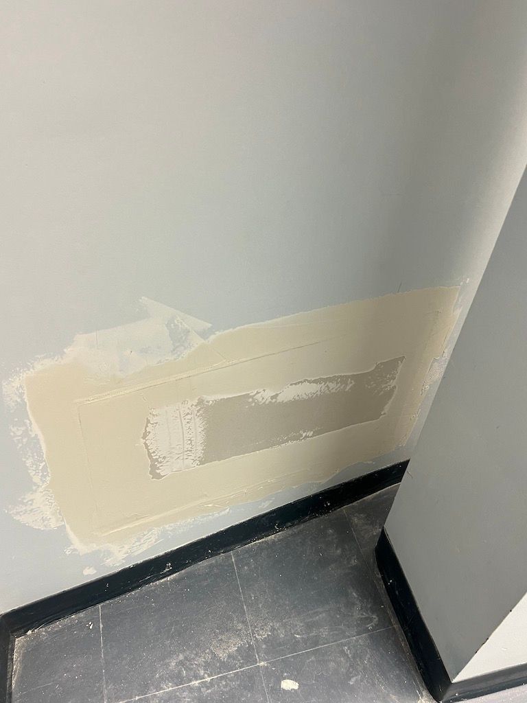Wall with a rough beige patch over damaged paint near a dark floor corner