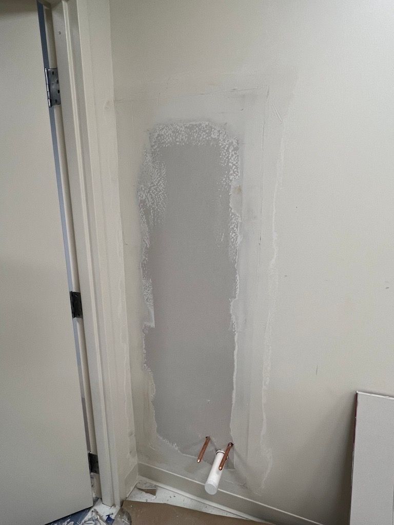 Patched drywall beside a door, with gray compound and a small putty knife on the floor
