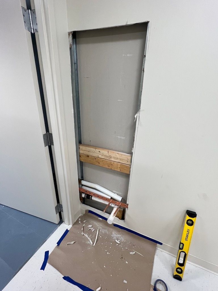 Open wall cavity with exposed framing beside a yellow level and protective floor covering.