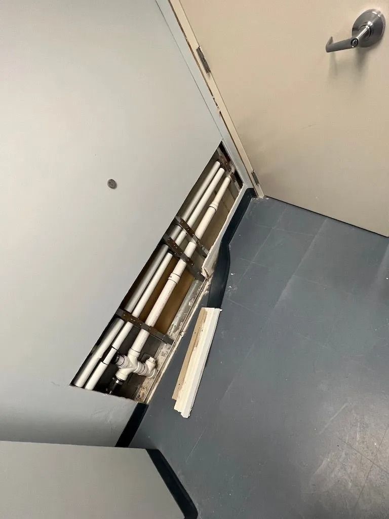 Tilted view of a white door and gray floor in a hallway, with a wall-mounted fixture and railing.