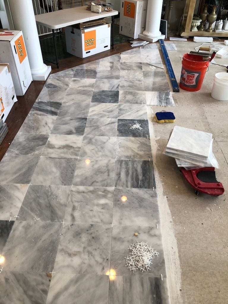 Marble flooring under installation beside a red bucket and tools in a home interior
