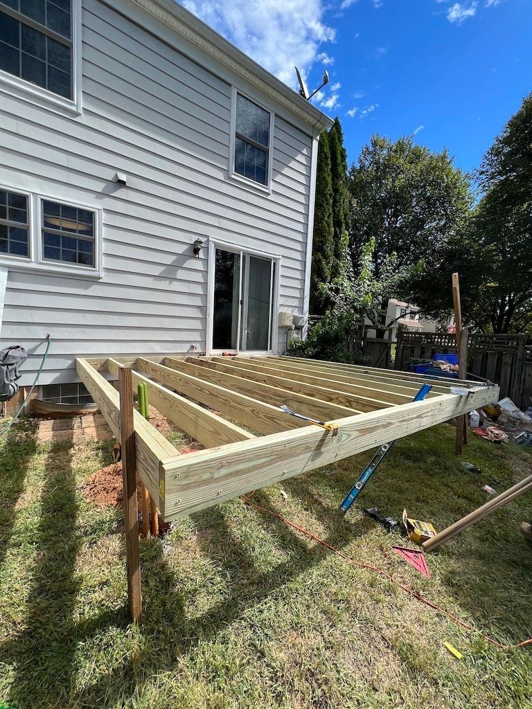 Wooden deck frame under construction beside a gray house in a sunny backyard