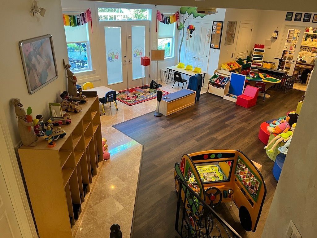 Colorful preschool classroom with toys, shelves, tables, and a bright play area by the windows