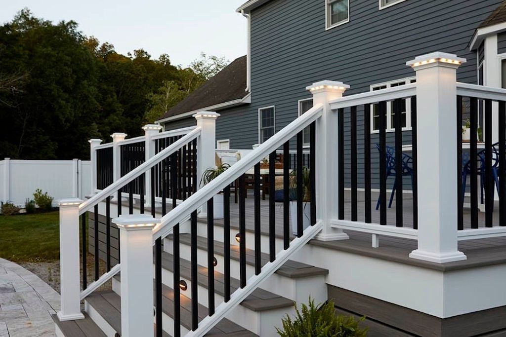 Outdoor home staircase with white railings and black balusters beside a gray house