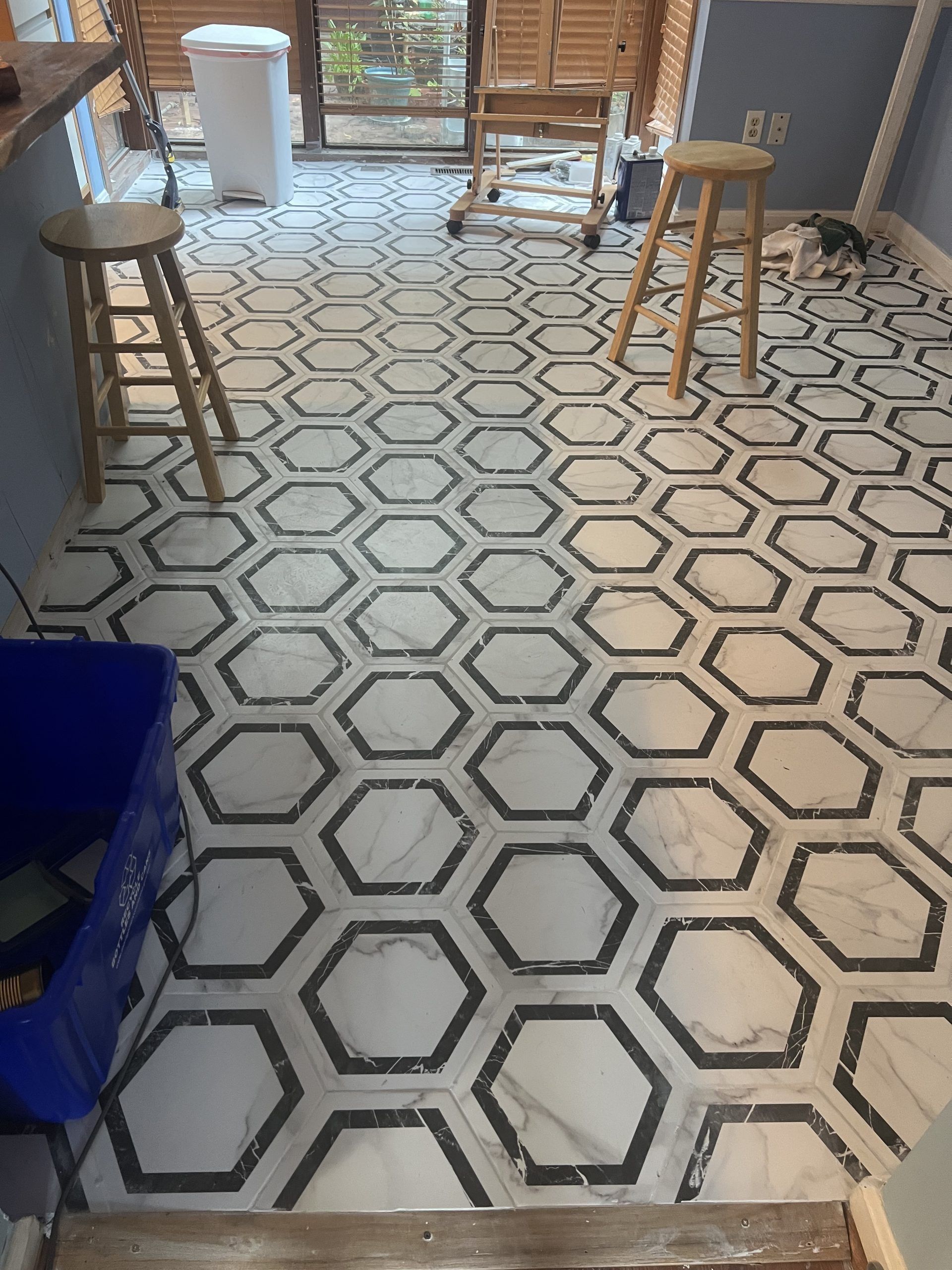 White hexagon-pattern tile floor in a room with stools and a glass door.
