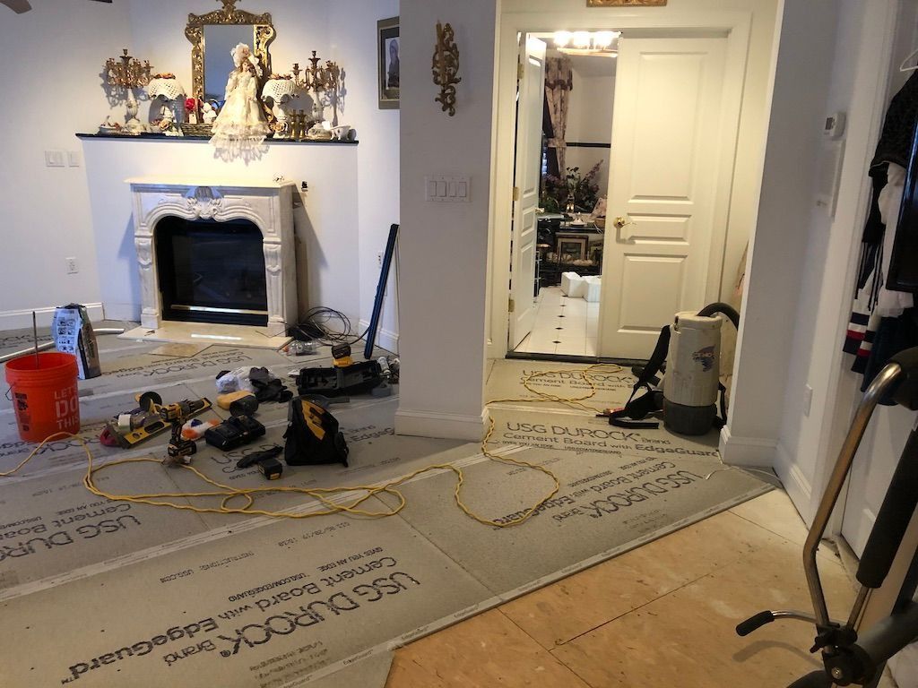 Living room renovation with tools, ladder, and debris around a white fireplace and open doorway