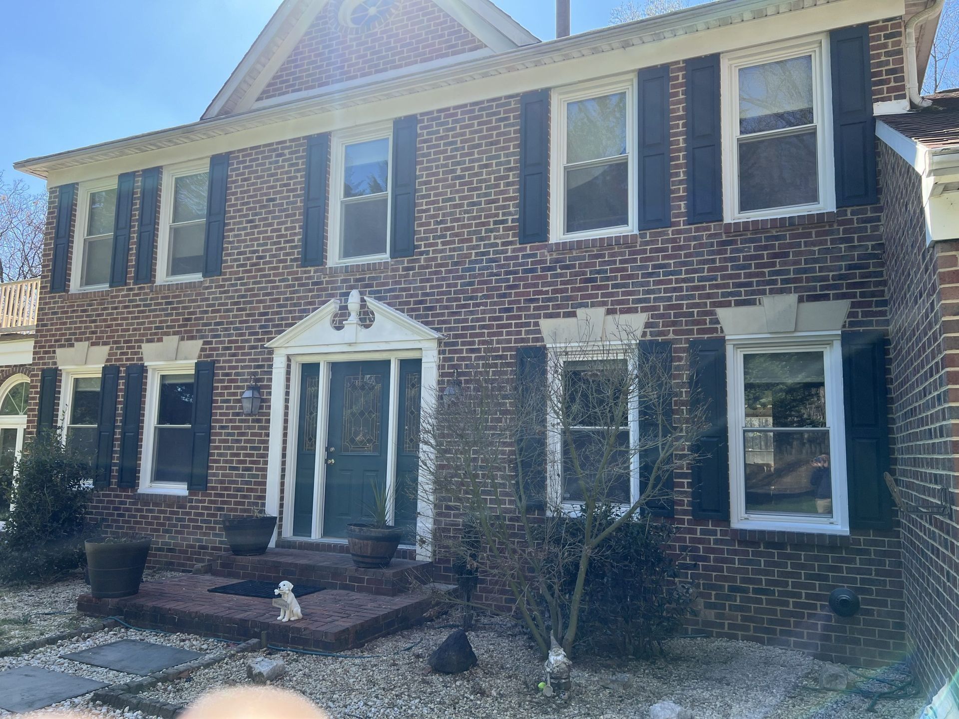 Brick two-story house with white-trimmed windows and a front entry on a sunny day