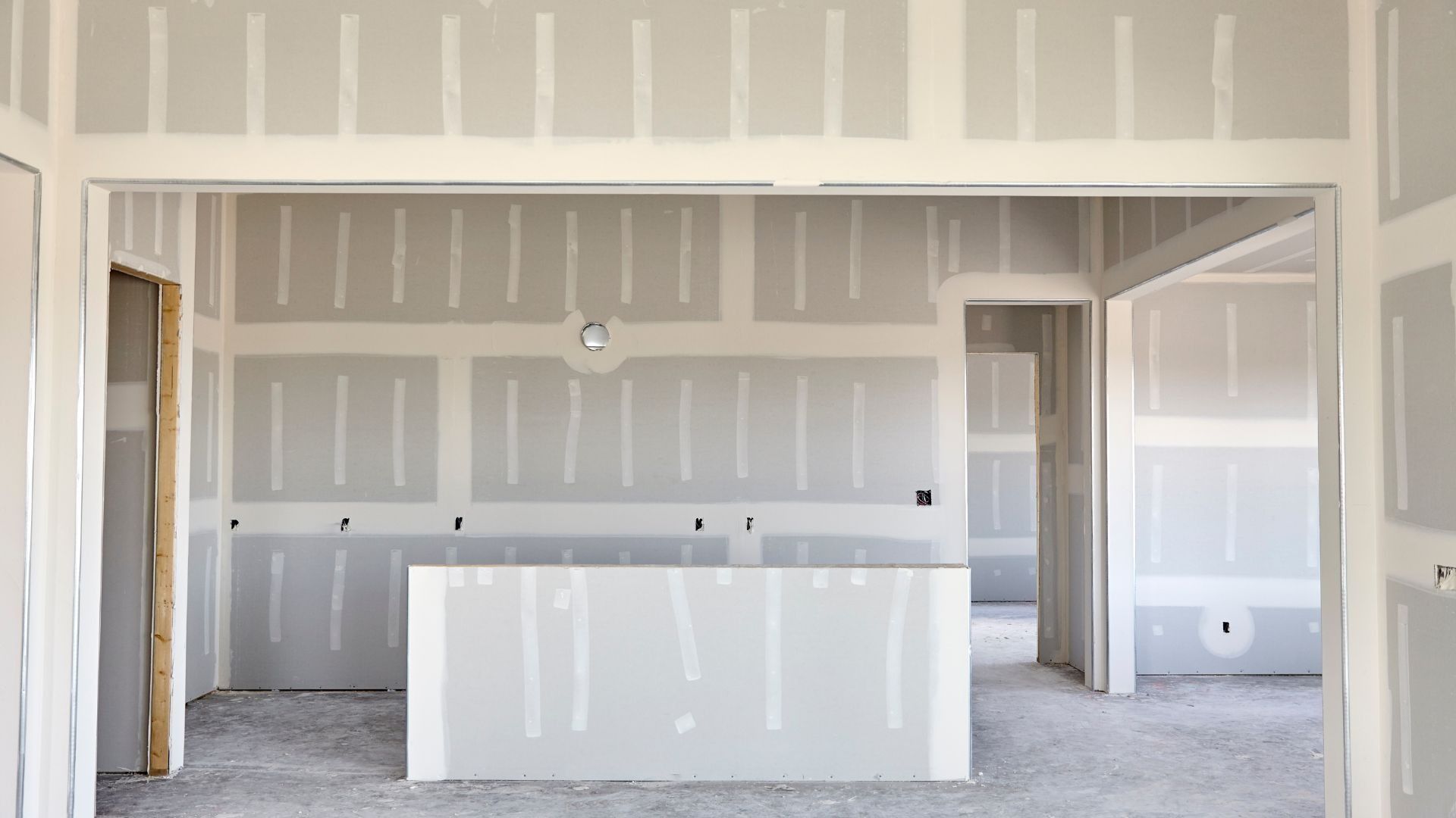 Unfinished drywall interior with a large kitchen island, open doorways, and exposed framing.