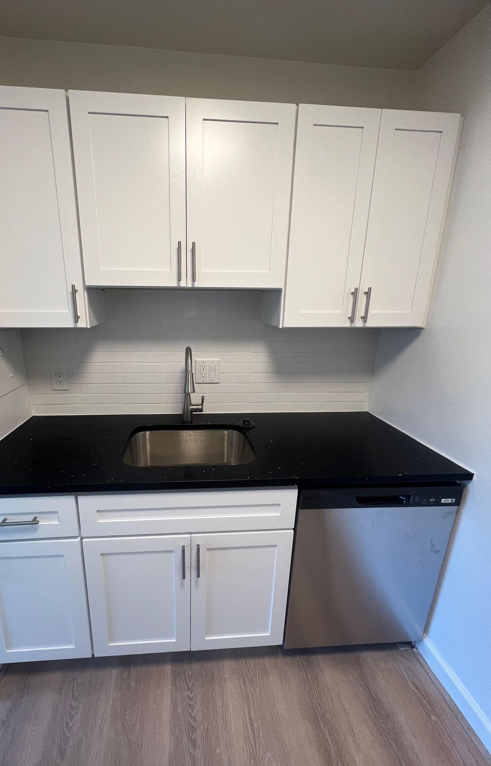 Small modern kitchen with white cabinets, black countertops, stainless sink, and a dishwasher.