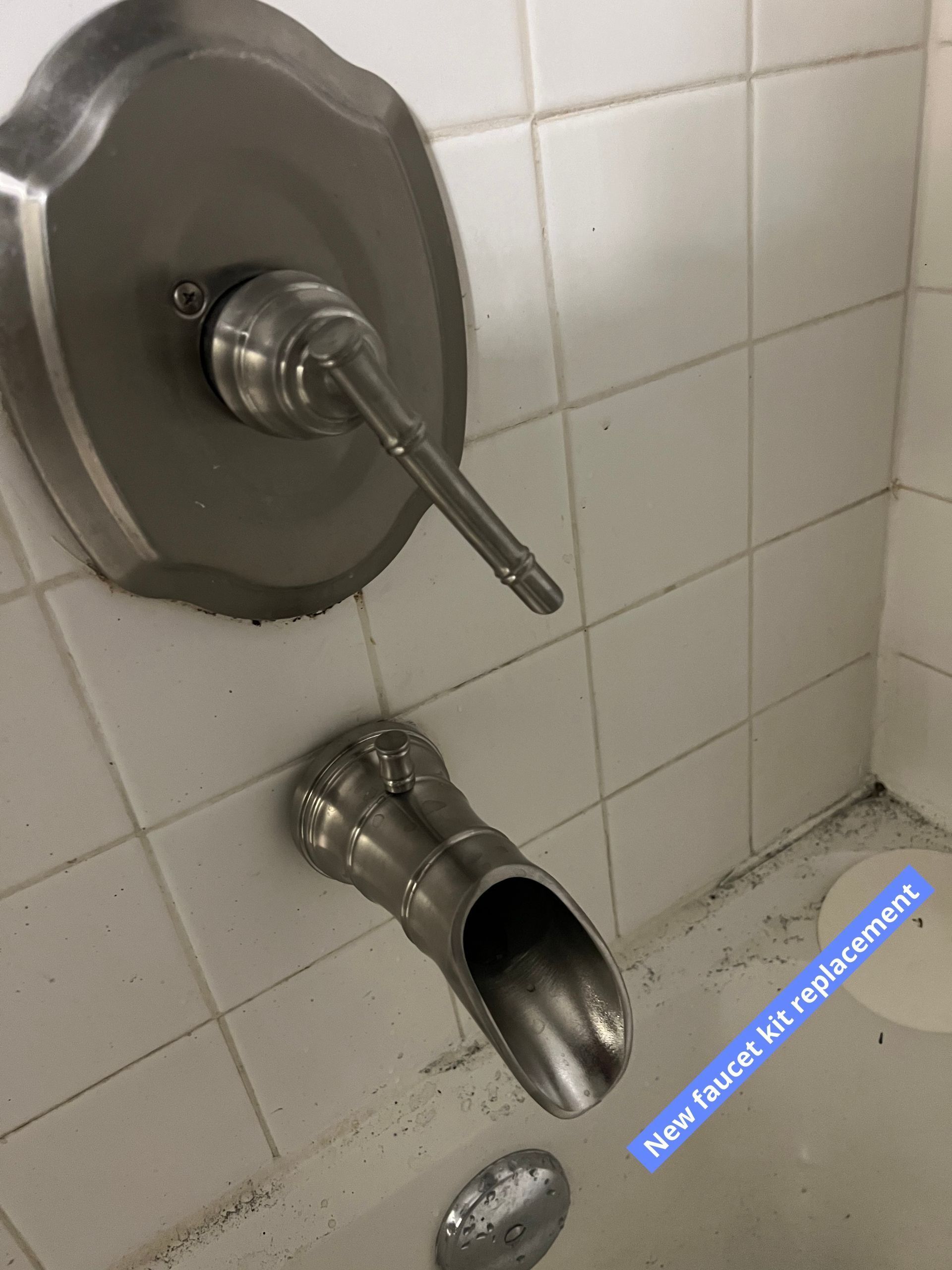 Broken wall-mounted shower faucet and pipe in a tiled bathroom, with a loose metal cover on the floor