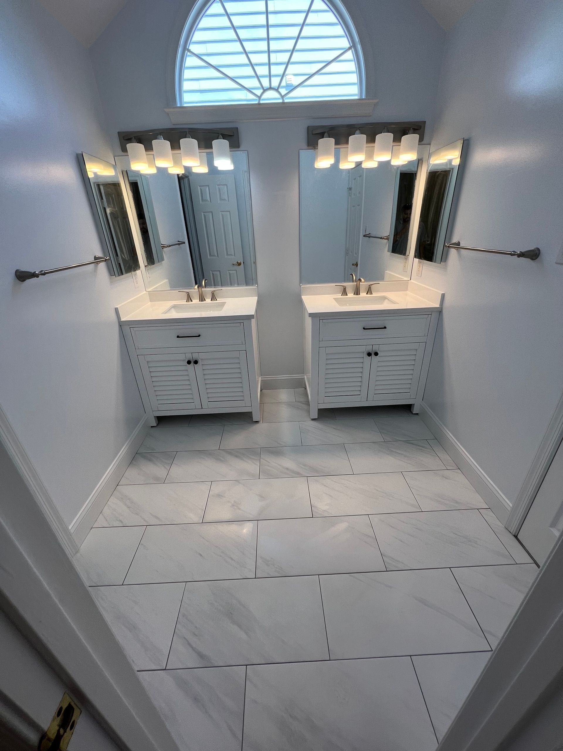 Bright white double vanity bathroom with mirrors, lights, and tiled floor