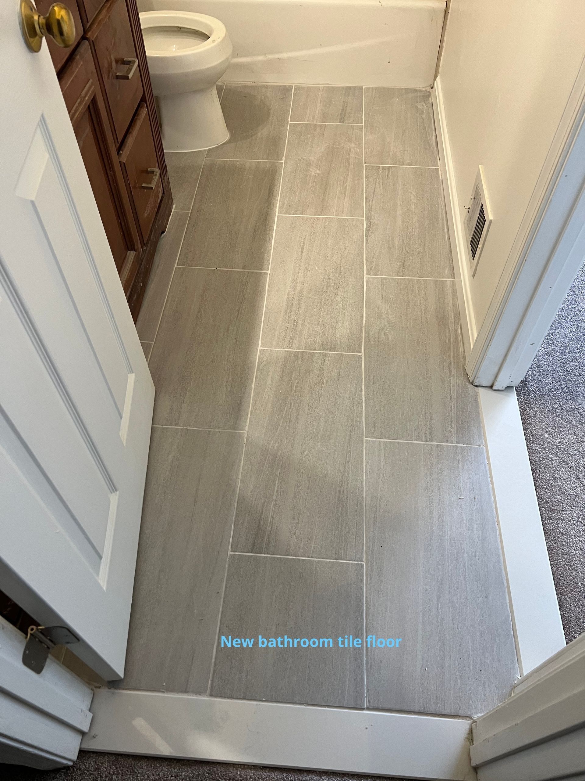 Narrow bathroom with gray tile floor, white toilet, vanity, and open doorways