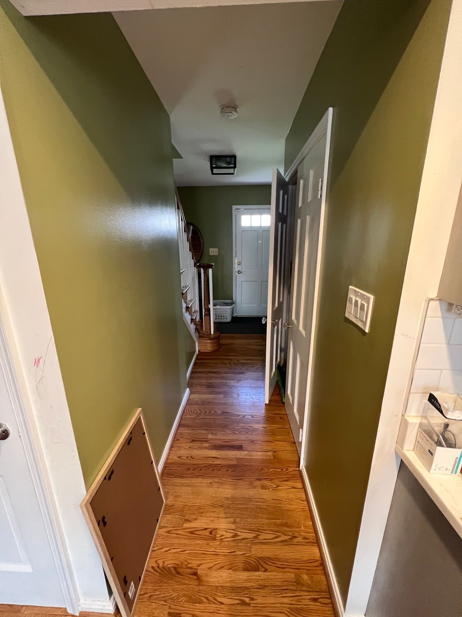 Narrow hallway with green walls, hardwood floor, and a white door at the end.