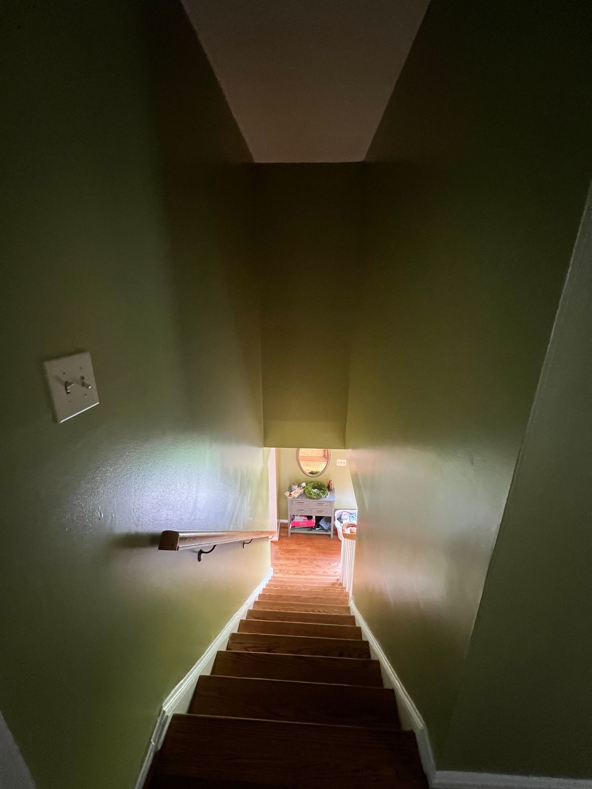 Narrow staircase descending to a lit landing in a dim green-walled interior