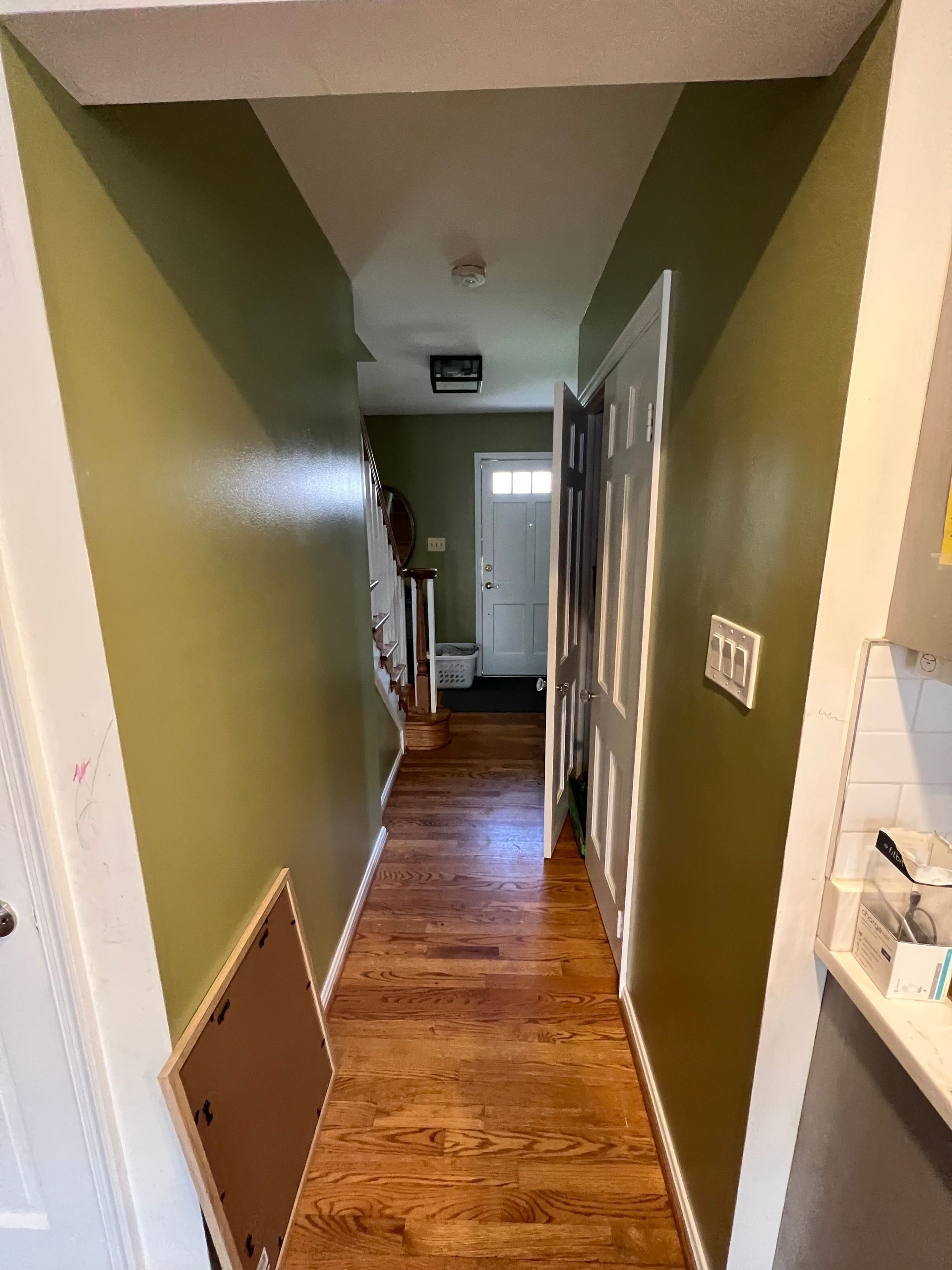 Narrow hallway with green walls and wood floor, leading to a bright room at the end.