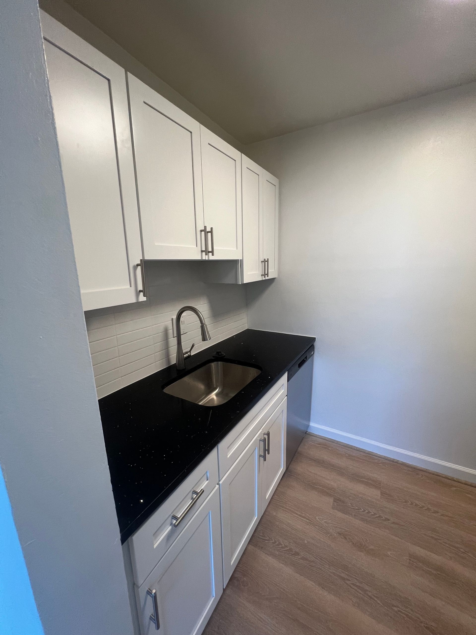 Small kitchen with white cabinets, black countertop, stainless sink, and wood flooring.