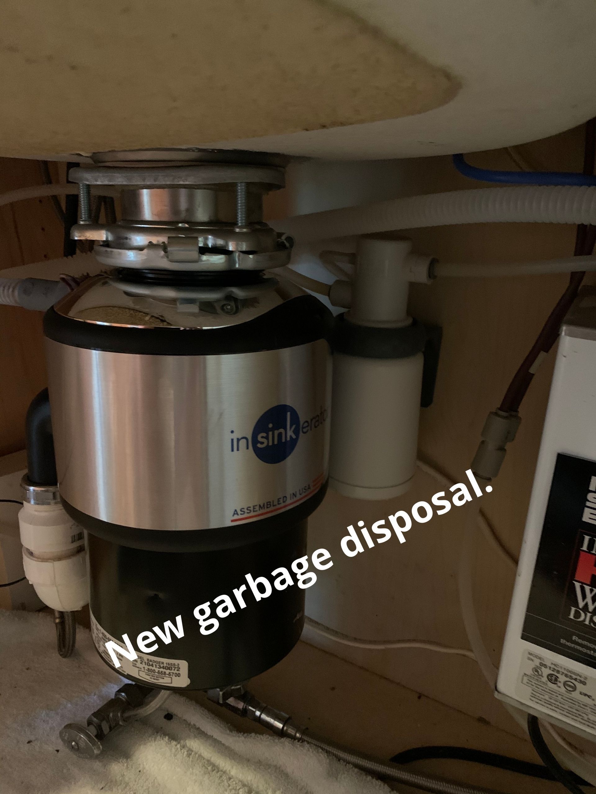 Under-sink garbage disposal mounted beneath a countertop, with a “New garbage disposal!” label.