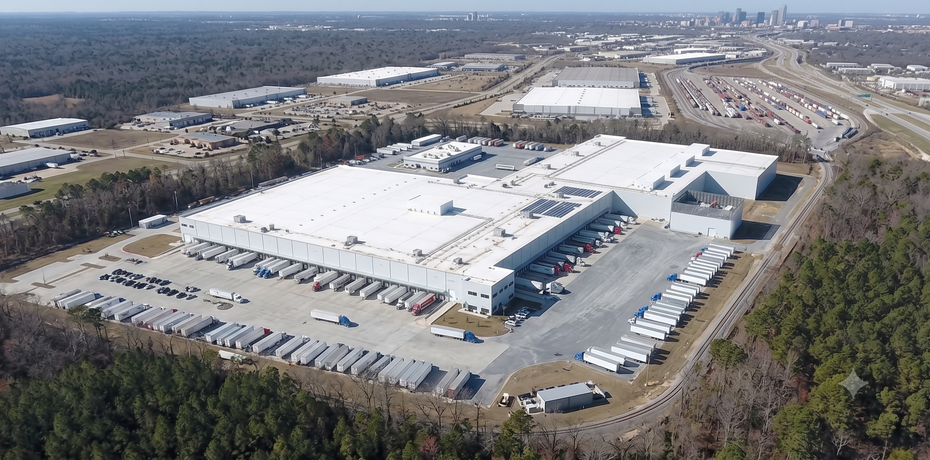 Aerial view of a large white industrial warehouse complex with parking lots and surrounding roads.