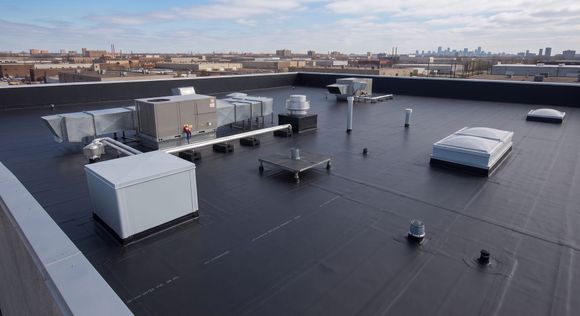Rooftop with HVAC units and vents on a flat black roof, city skyline in the distance.