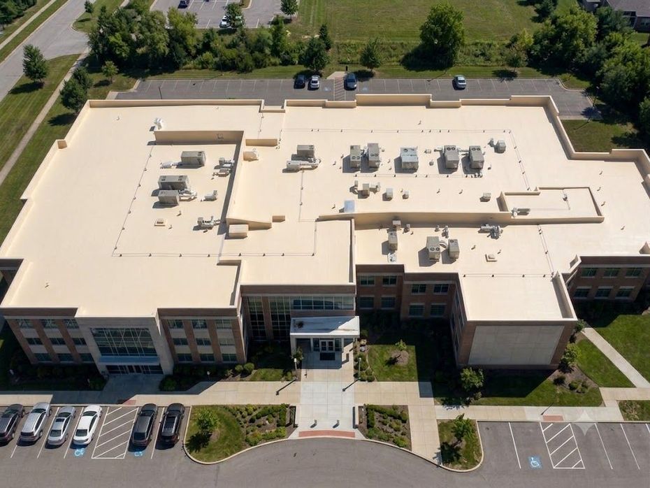Aerial view of a large beige office building with rooftop equipment and parking lot below