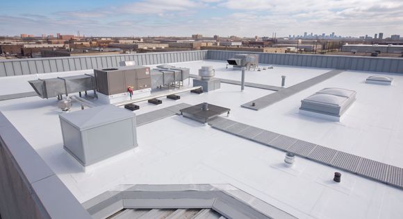 Snow-covered industrial rooftop with HVAC units and vents under a bright sky.