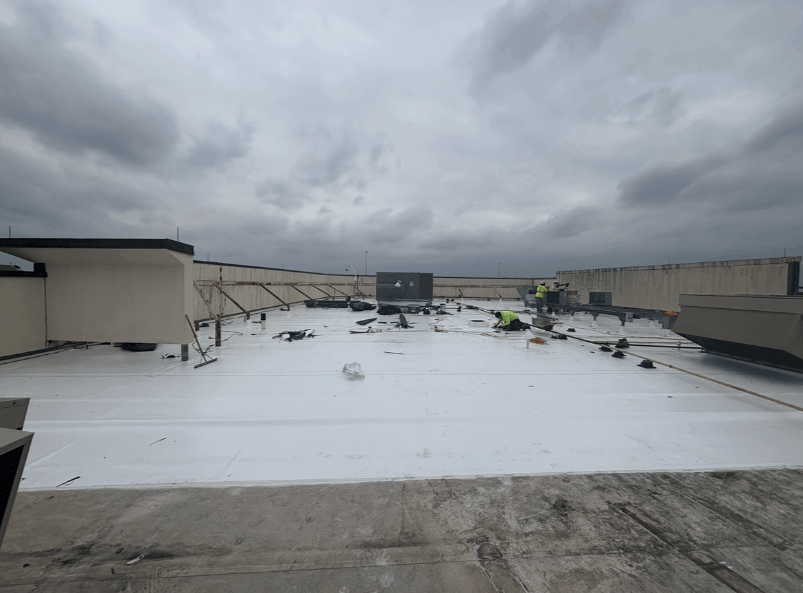 Snow-covered rooftop with two workers under a gray cloudy sky, damaged panels visible near the right side.